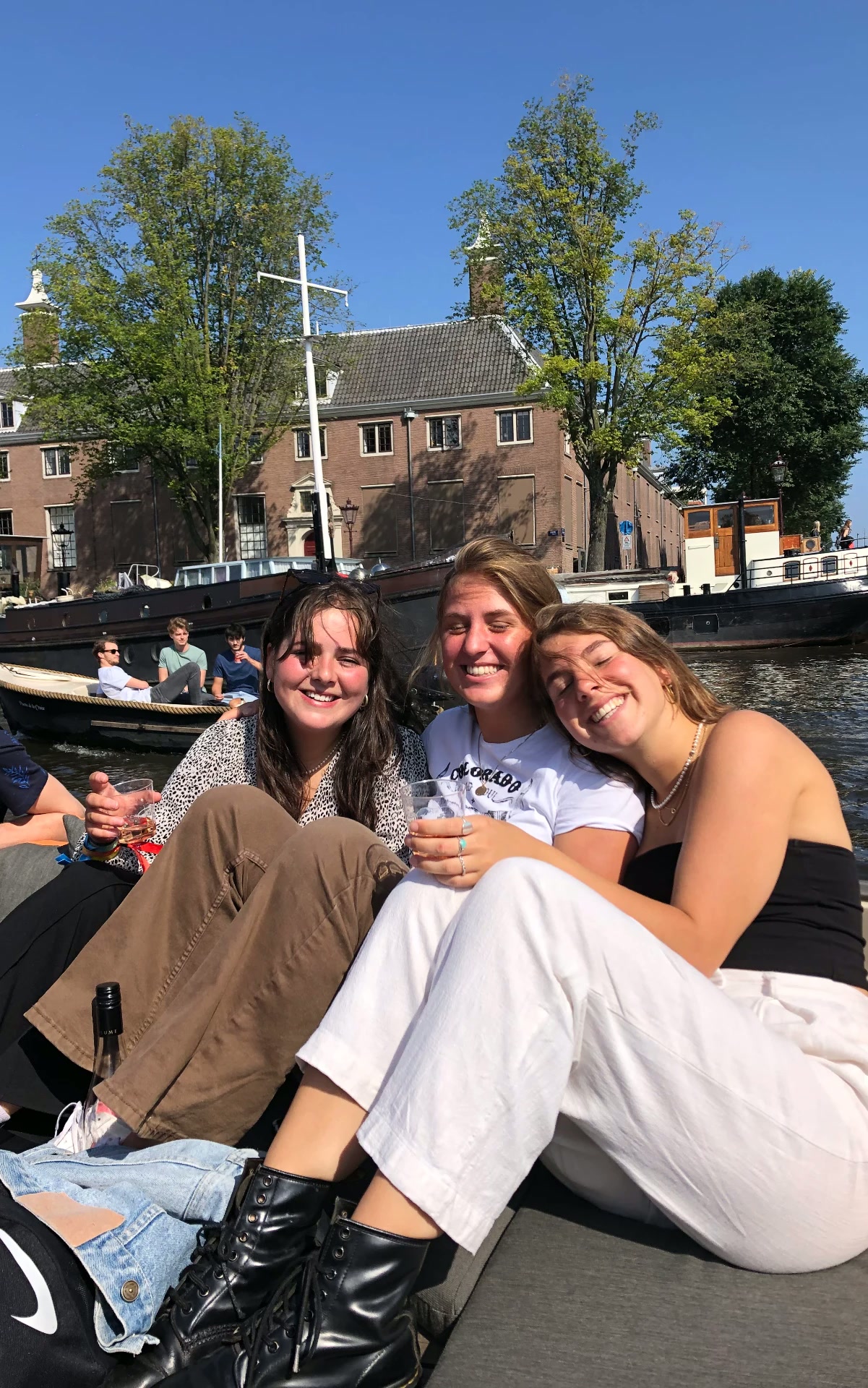 Drie vrienden lachend op een boot in een Amsterdamse gracht op een zonnige dag