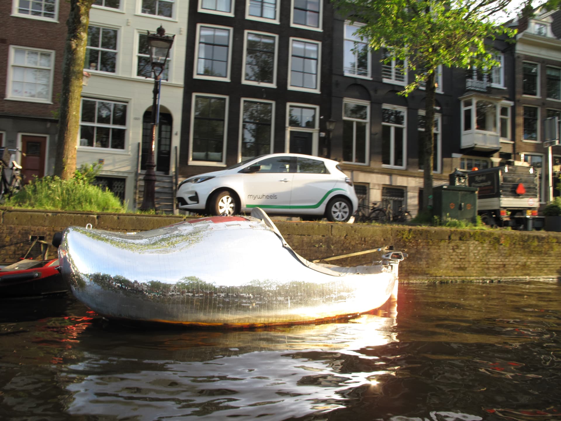 A boat covered in mirror tiles moored along the canal in low sun