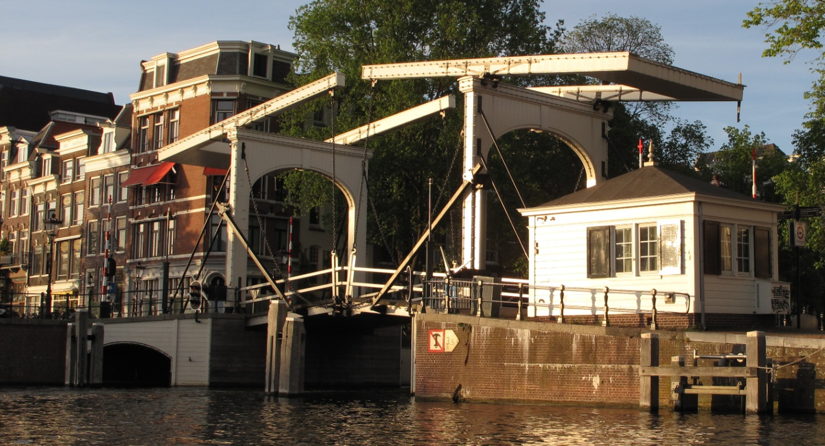 Een geopende ophaalbrug over een Amsterdamse gracht, gezien vanaf een klein bootje