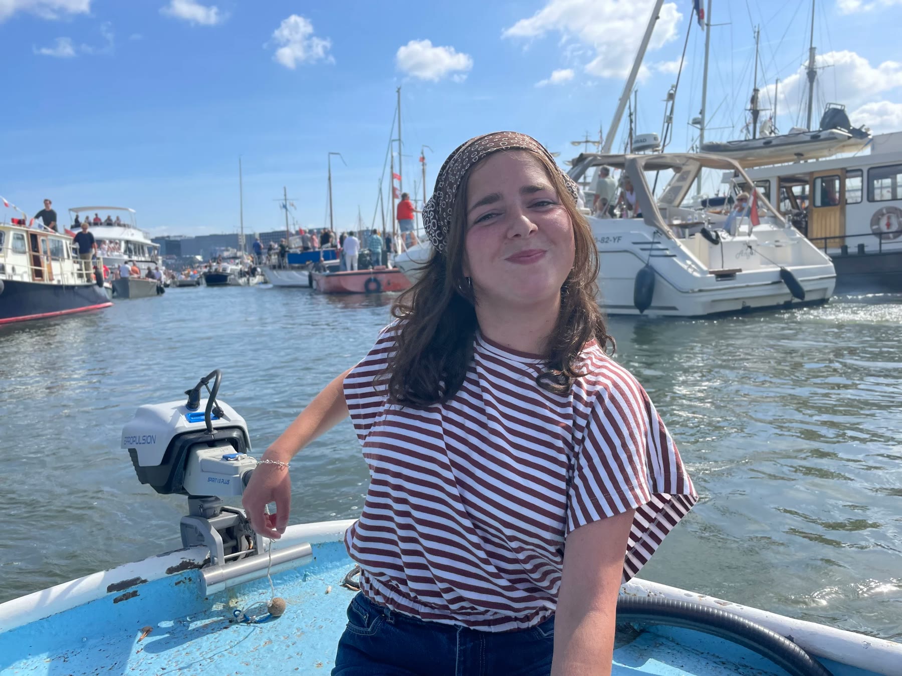 Isabelle aan het roer van haar boot, met tallships achter haar op het IJ